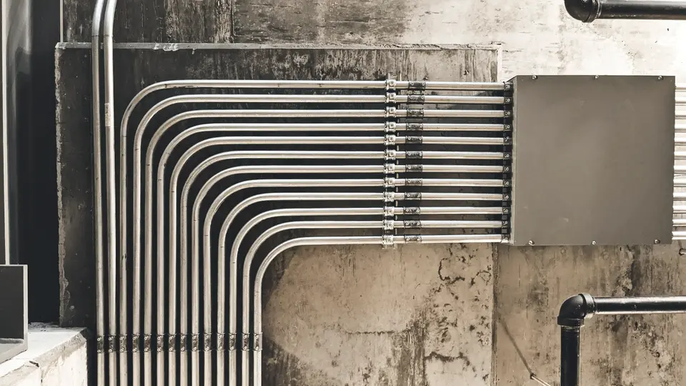 Rows of electrical conduit bending across a concrete wall into a junction box.